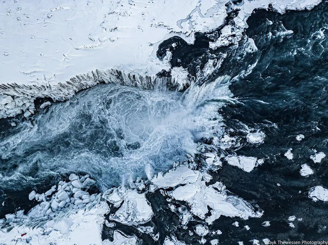 Top-down aerial of Dettifoss waterfall in winter, ice sheets fringing the dark glacial water