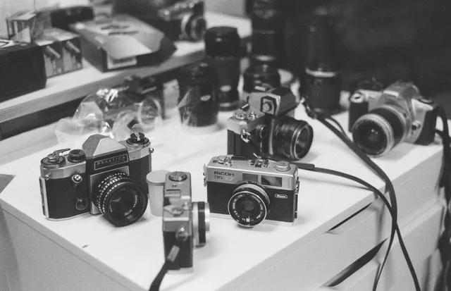 Black-and-white still of vintage film cameras and lenses gathered on a table