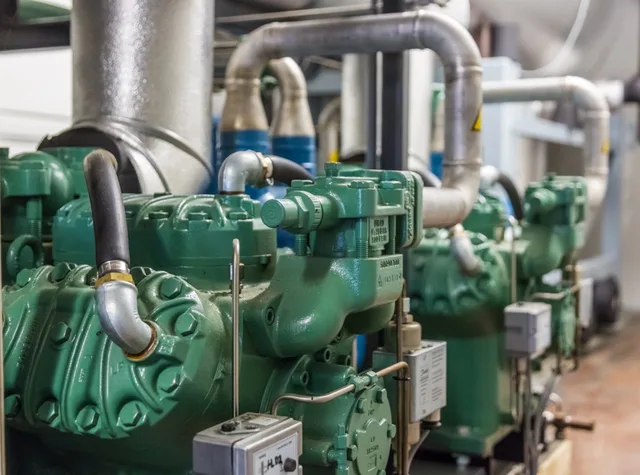 Green refrigeration compressors and piping inside an industrial plant room