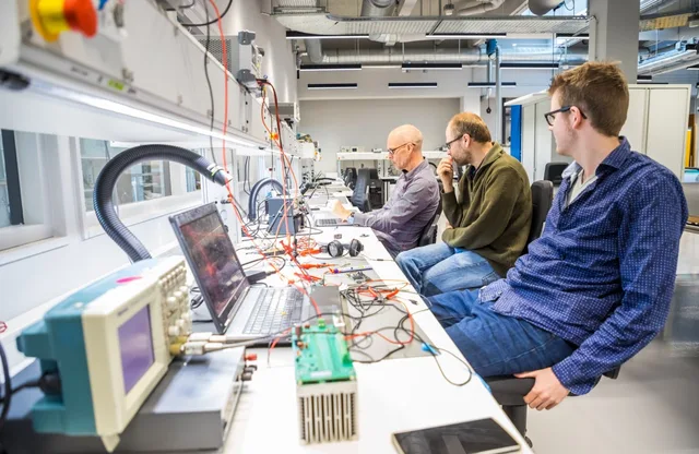 Engineers testing power electronics at a lab bench with oscilloscopes and prototype boards