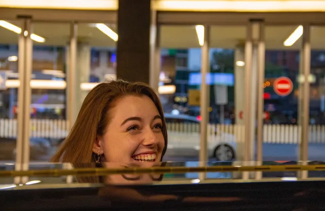 Woman smiling over a car window at dusk, evening street traffic blurred behind her