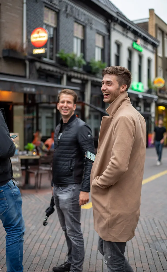 Two men bursting out laughing on a bar-lined street in the evening