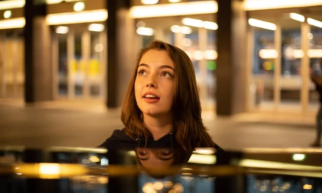 Young woman looking up from behind the lid of the public station piano at Eindhoven Centraal at night