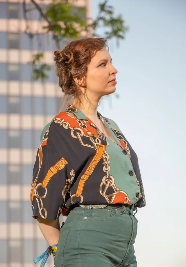 Profile portrait of a woman in a patterned blouse, hair pinned up, against a glass high-rise