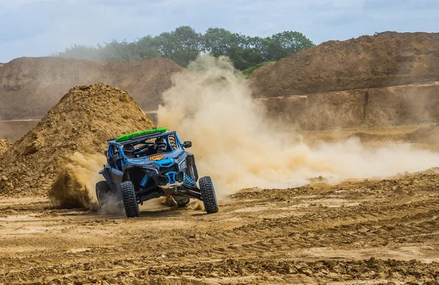 Side-by-side buggy drifting through a sand quarry, dragging a wall of dust behind it