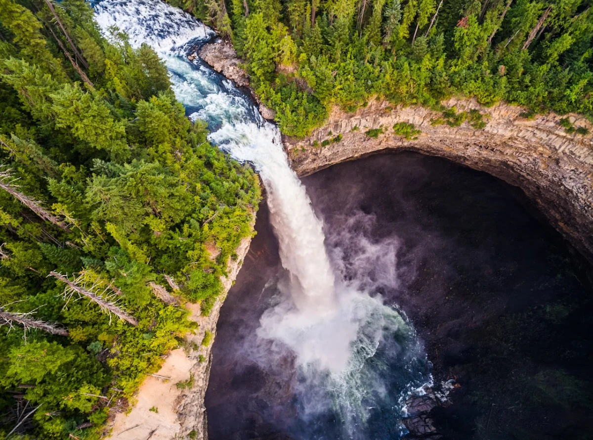 Aerial drone photo looking straight down a waterfall plunging into a canyon pool surrounded by forest
