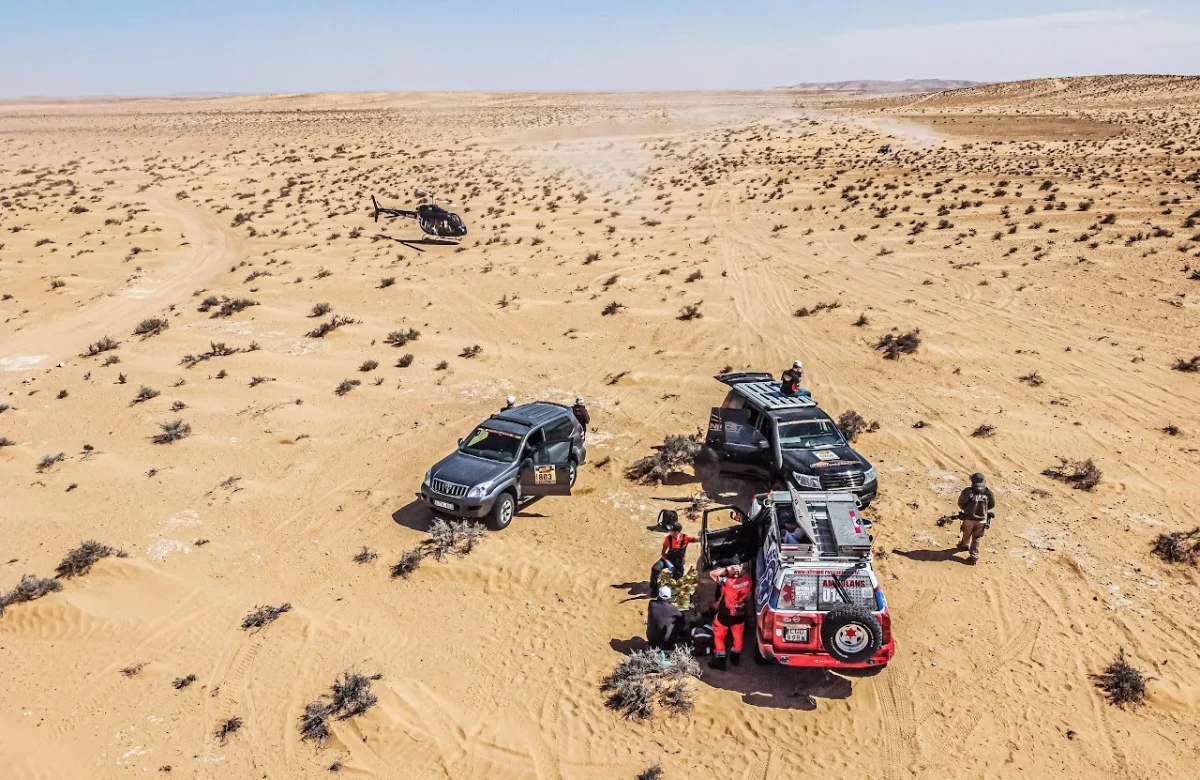 Desert rally scene from the air: helicopter, support trucks and crews on the sand